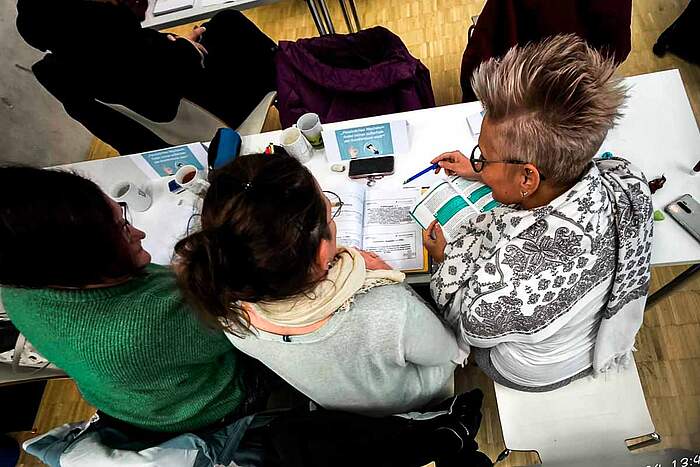 Weiterbildung zur Praxisanleiterin Dei drei angehenden Praxisanleiterinnen an ihrem Schultisch mit vielen Unterlagen vor sich.