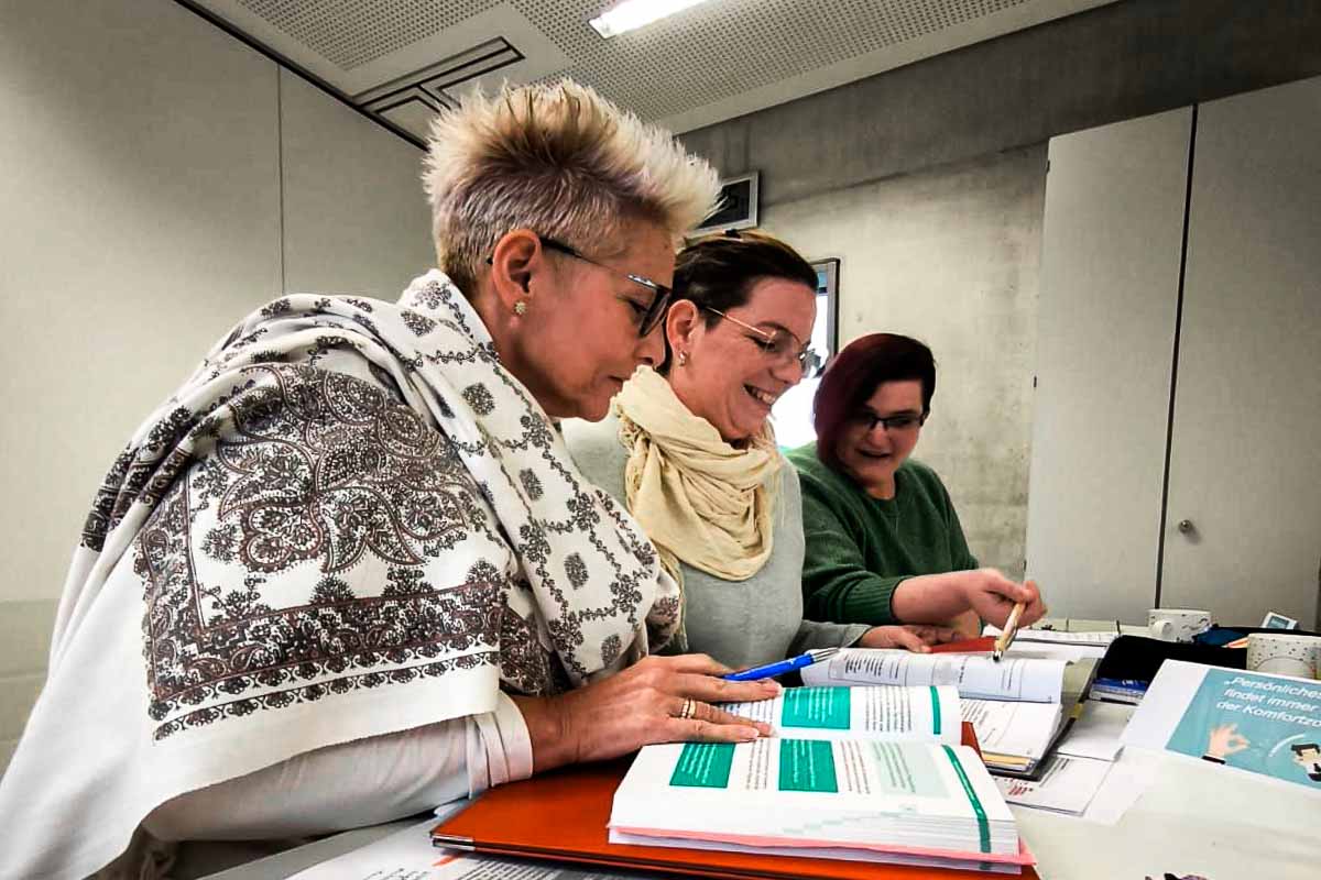 Weiterbildung zur Praxisanleiterin bei de rEvangelischen Sozialstation Mosbach. Dei drei angehenden Praxisanleiterinnen an ihrem Schultisch mit vielen Unterlagen vor sich.